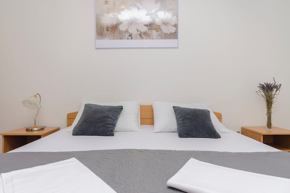 A neatly made bed with white and gray bedding, two bedside tables with lamps, and a wall-mounted artwork of flowers.