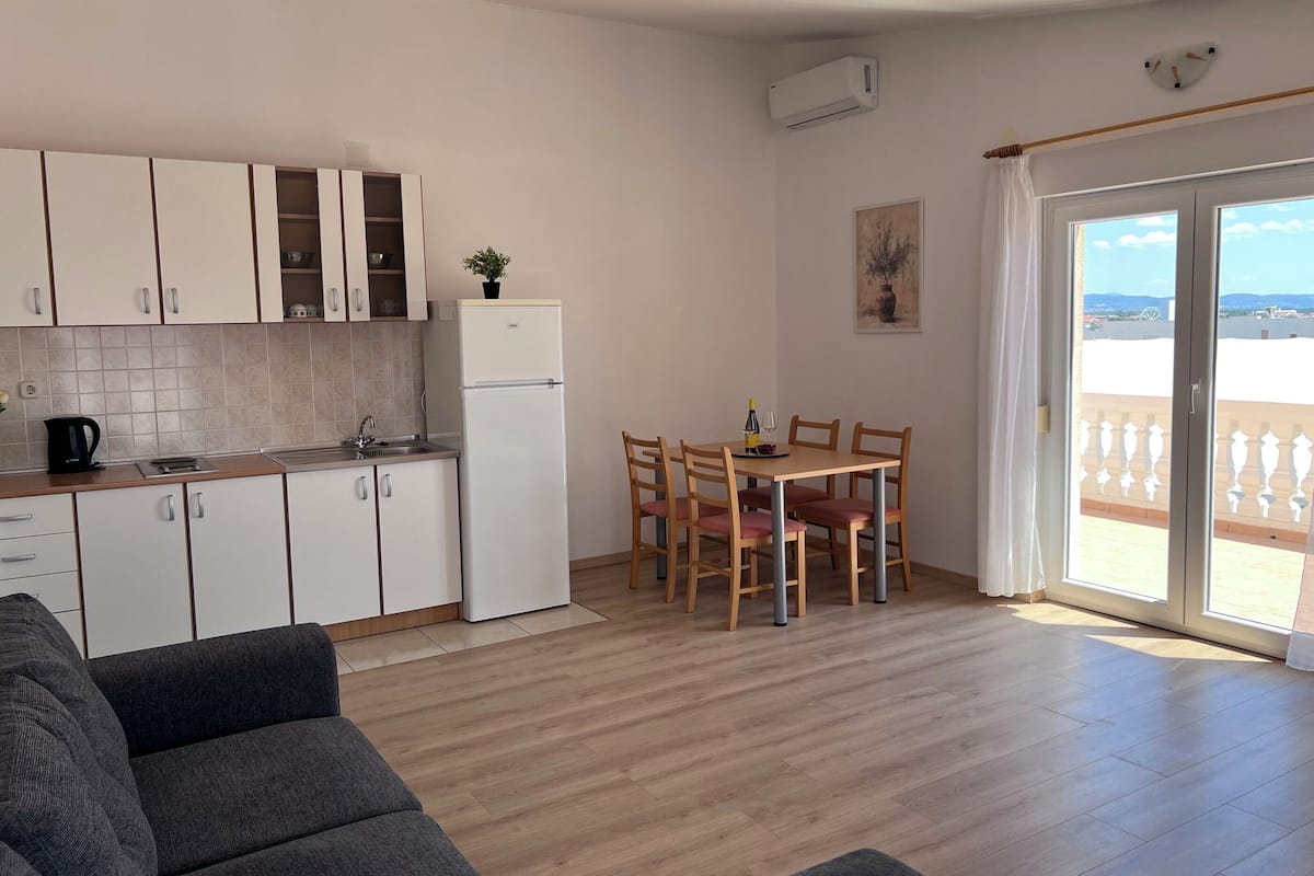 A modern kitchen with white cabinets, a refrigerator, and a dining area with wooden chairs and a table.
