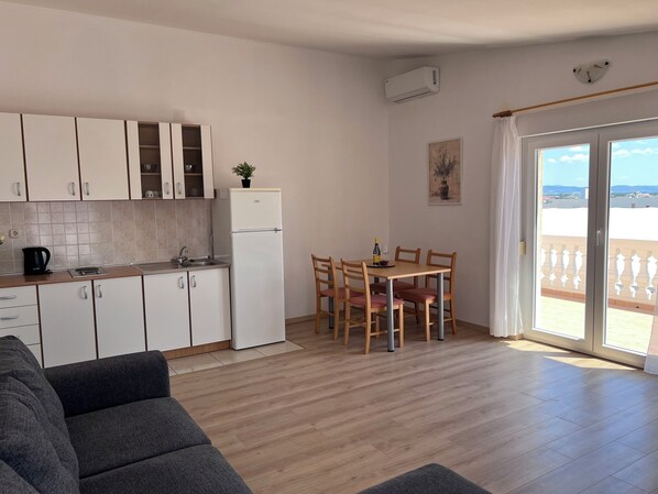 A modern kitchen with white cabinets, a refrigerator, and a dining area with wooden chairs and a table. - Apartments Sabina (Vodice)