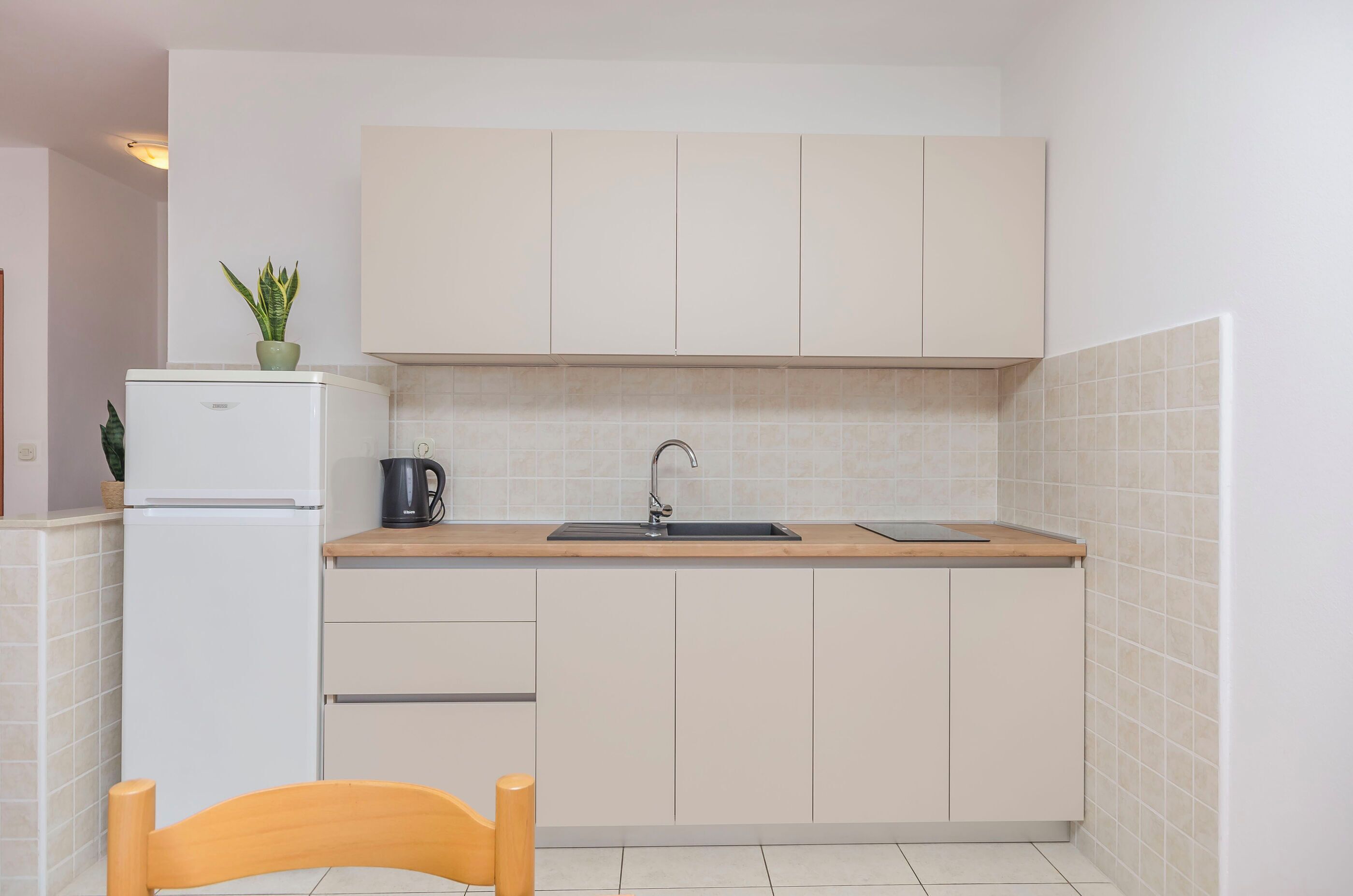 A compact kitchen with a sink, a kettle, and a refrigerator.