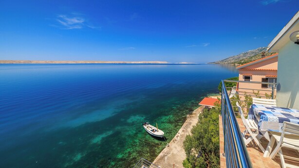 A balcony with a view of a calm sea, a boat, and a building with a red roof. - Apartment Toma (Karlobag)