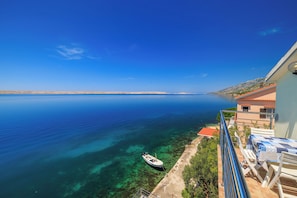 Ein Balkon mit Blick auf ein ruhiges Meer, ein Boot und ein Gebäude mit rotem Dach.