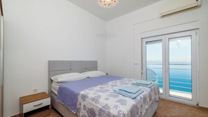 A bedroom with a bed, a nightstand, a window with a view of the sea, and an air conditioning unit. - Apartment Toma (Karlobag)