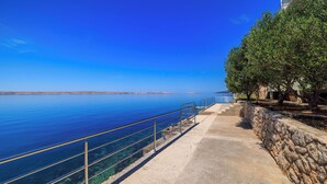 A coastal walkway with a clear view of the sea, a stone wall, and a metal railing. - Apartment Toma (Karlobag)
