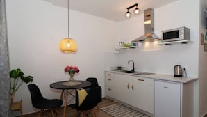 A compact kitchen with a microwave, sink, and cabinets. There is a dining table with chairs and a hanging light fixture. - Apartments Edvard (Split)