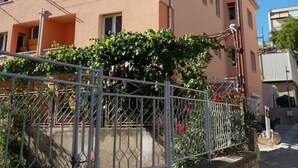 A two-story building with a flat roof, a metal fence, and a small garden with red flowers. - Apartments Edvard (Split)