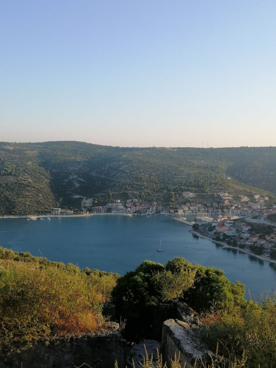 Uma cidade costeira com uma baía, cercada por colinas e vegetação.