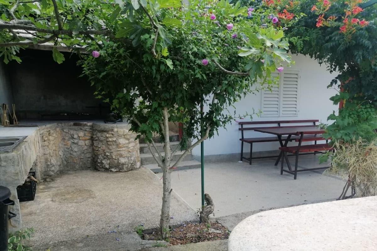 A patio area with a stone wall, a small tree, a wooden table, and a bench.