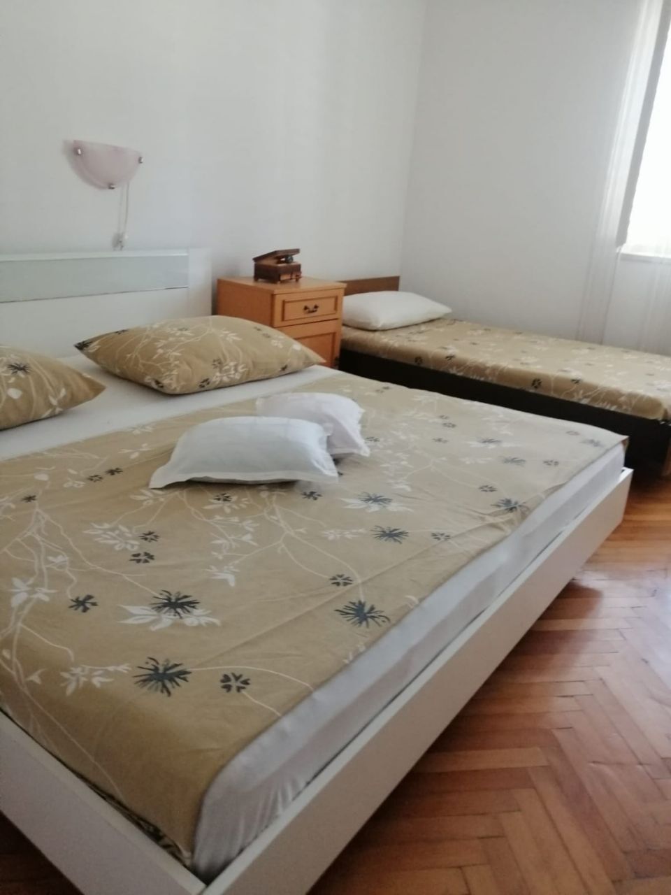 Un dormitorio con dos camas individuales, una mesita de noche de madera, un aparador pequeño y una lámpara de pared.