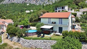 A two-story house with a red-tiled roof, a swimming pool, and a stone wall. - Apartment Ivo (Tucepi)