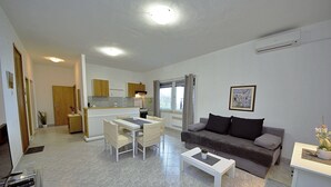 A modern living room with a grey sofa, a white coffee table, and a dining area with a white table and chairs. - Apartment Ivo (Tucepi)
