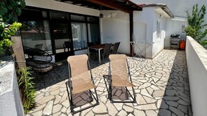 Un patio al aire libre con suelo de piedra, dos sillones, una mesa y una pérgola.