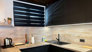 Una cocina moderna con encimera de madera, armarios negros, un lavabo negro y una ventana con persianas horizontales.