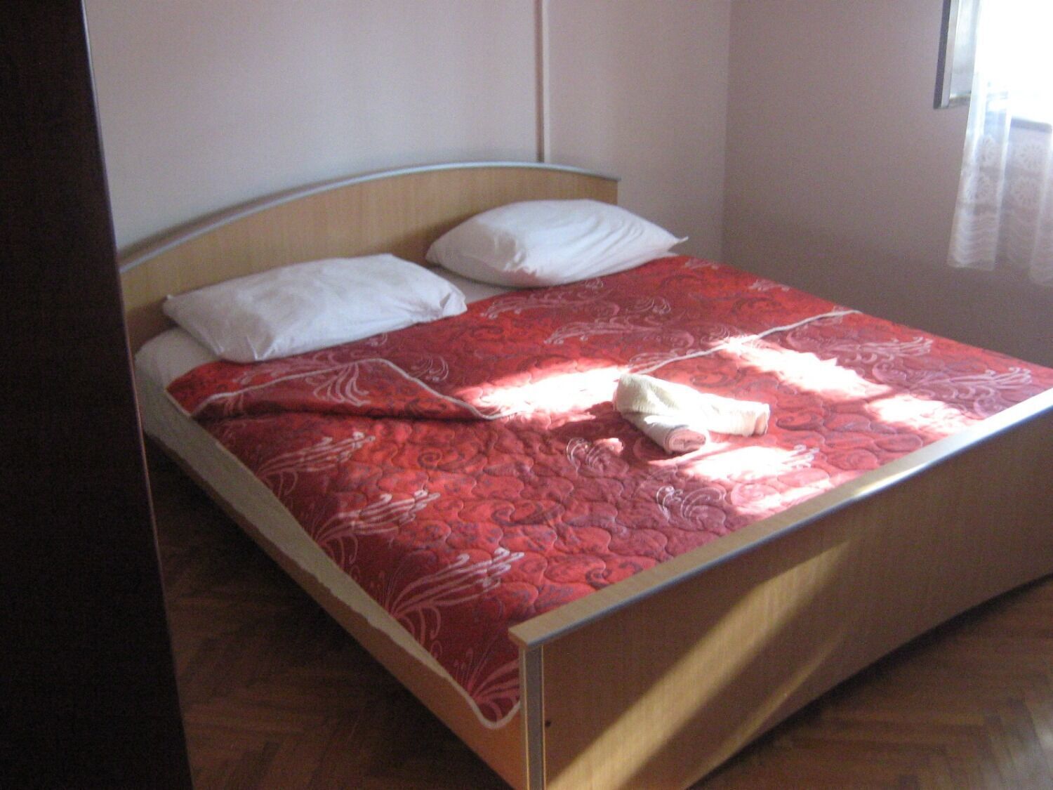 A single bed with a red patterned bedspread, two white pillows, and a wooden headboard.