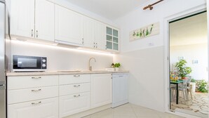 A modern kitchen with white cabinets, a microwave, a sink, and a dishwasher. - Apartment Bosiljka (Marina)