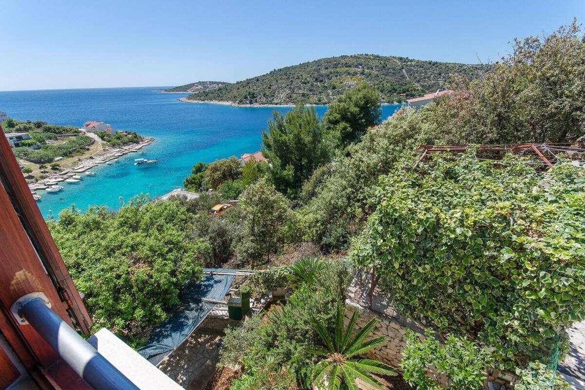 A coastal landscape with a clear view of the sea, a hillside with dense vegetation, and a stone wall.