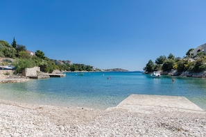 Una playa de guijarros con agua cristalina, barcos y casas a lo largo de la orilla.
