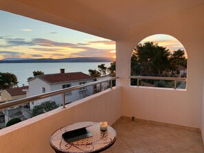 A balcony with a view of a sunset over water, a tiled floor, and a small table with a laptop and candle. - Apartment Sanda (Solta)