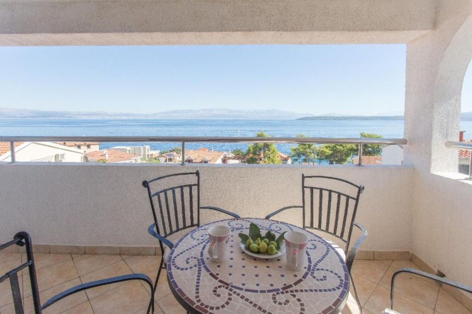 A balcony with a table and chairs, overlooking a coastal view.