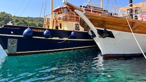 Ein großes Segelschiff liegt in einer Marina vor türkisblauem Wasser, im Hintergrund ein bewaldeter Hügel.
