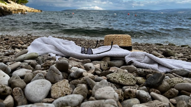 Ein felsiger Strand mit Sonnenhut, Sonnenbrille und Handtuch.