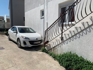 Ein weißes Auto vor einem Gebäude mit Metallgeländer und einem kleinen Fenster.