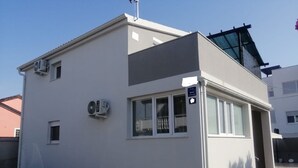 Un edificio moderno de una sola planta con techo plano, dos unidades de aire acondicionado y una ventana pequeña.