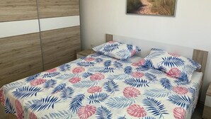 Un dormitorio con cama, armario de madera y colcha con motivos playeros.