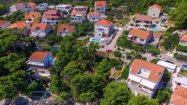 An aerial view of a coastal residential area with houses, a swimming pool, and clear turquoise waters. - House Sandra (Lumbarda)