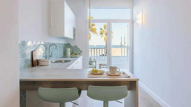 Een keuken met een centraal eiland, twee barkrukken, een spoelbak en uitzicht op het strand door grote ramen.