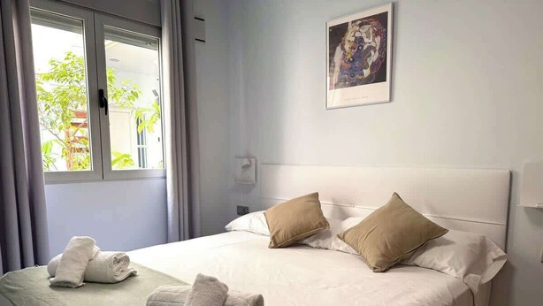 Habitación de hotel con cama, dos almohadas, ventana con cortinas e imagen en el marco en la pared.