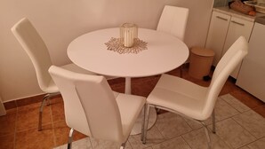 A round white table with four white chairs, a decorative glass centerpiece, and a tiled floor. - Apartment Bubi (Solta)