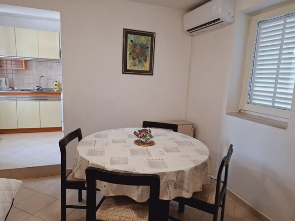 Un coin repas avec une table ronde recouverte d’une nappe blanche, entourée de quatre chaises. Une œuvre d’art encadrée est accrochée au mur au-dessus de la table.