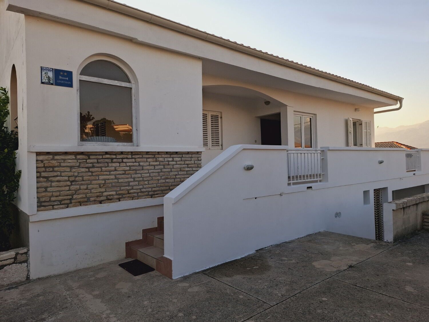 Ein Gebäude mit einer Steinauffassung, einer Treppe, die zu einem überdachten Eingang führt, und einem Schild, das es als kroatische Wohnung kennzeichnet.