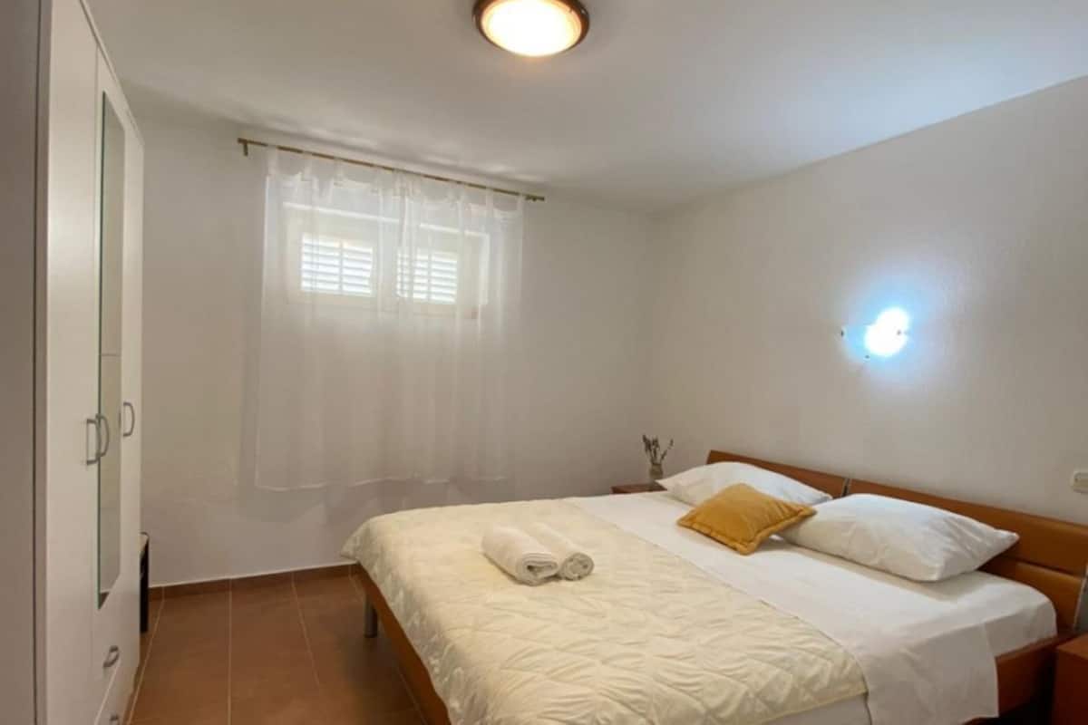 Une chambre à coucher comprenant un lit, une table de chevet, une armoire et une fenêtre avec des rideaux.