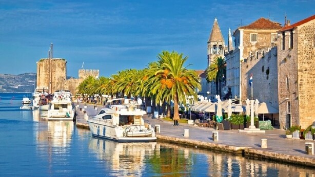 A waterfront marina with boats docked, a historic stone building, and palm trees lining the promenade. - Apartment Vesna (Trogir)