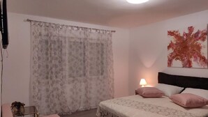A bedroom with a bed, a nightstand, a lamp, a TV, and a window with curtains. - Apartments Rosa (Split)