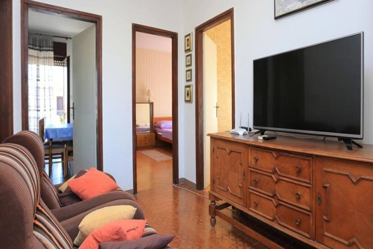 A living room with a sofa, a TV on a wooden cabinet, and a door leading to another room.