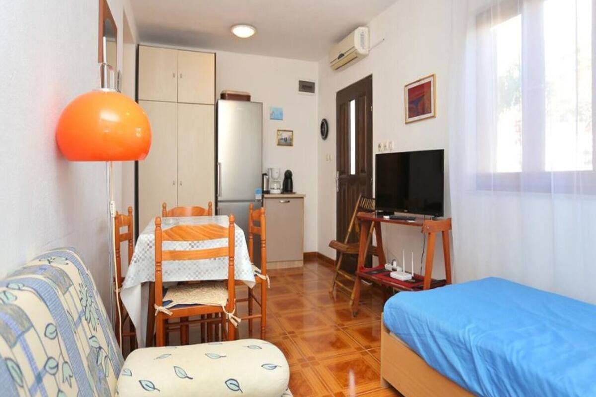 A compact room with a bed, a small table with chairs, a television, and a kitchenette.