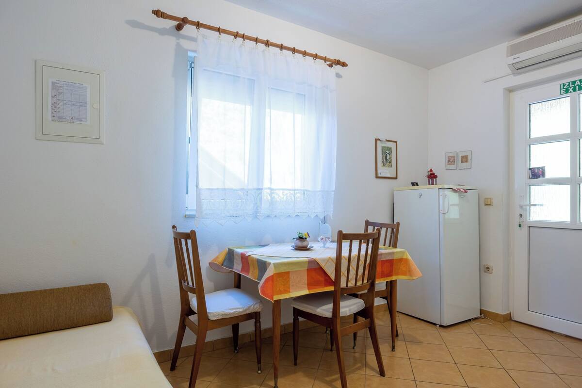 Ein kleiner, sauberer Raum mit einem Bett, einem Tisch mit Stühlen, einem Kühlschrank und einem Fenster mit Vorhängen.