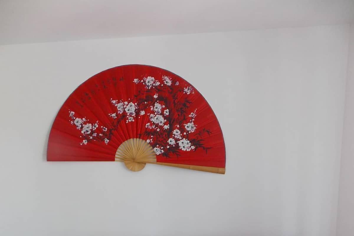 A red leather sofa with a cushion and a decorative red fan with floral patterns on the wall behind it.