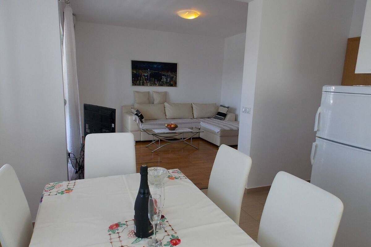 A dining area with a table set for two, a sofa, a coffee table, and a refrigerator.