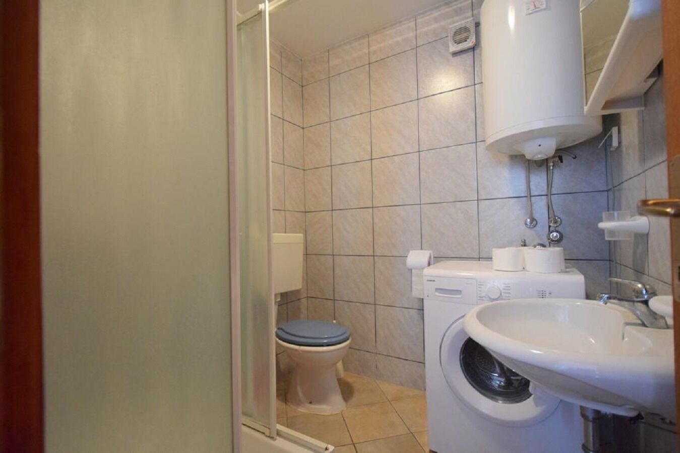 A small bathroom with a toilet, a washing machine, and a sink.