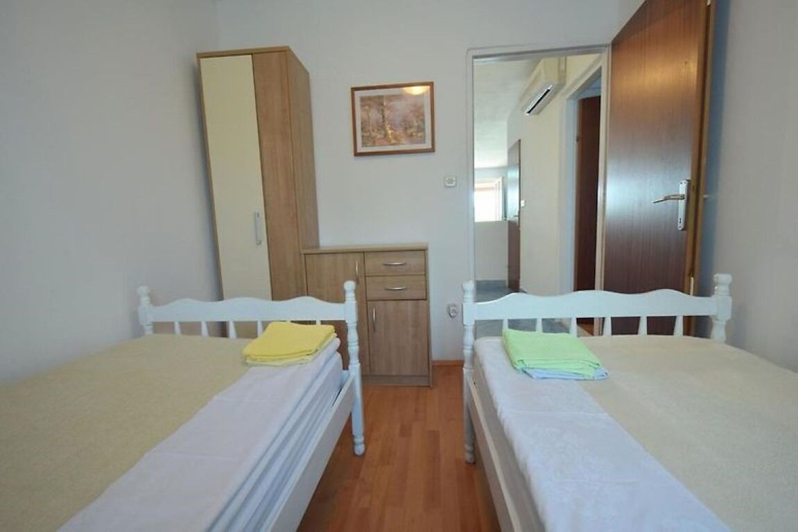 A bedroom with two single beds, a wooden wardrobe, a small desk, and a mirror.