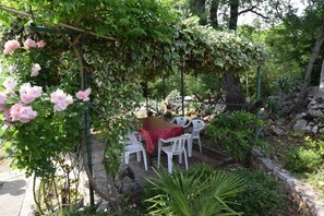 Un área de estar al aire libre con una mesa y sillas, rodeada de vegetación y una pérgola con plantas trepadoras.