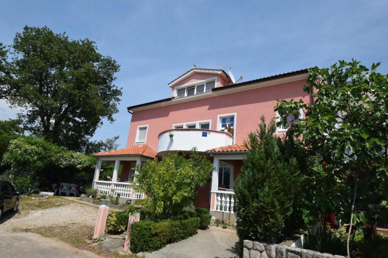A two-story building with a pink facade, a balcony, and a stone wall in front.