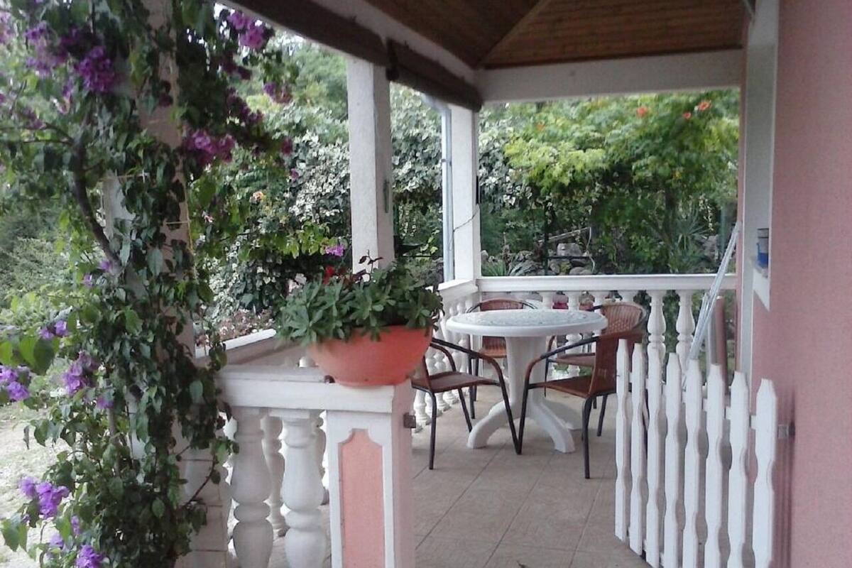 A covered outdoor patio with a round table and chairs, surrounded by a white picket fence.