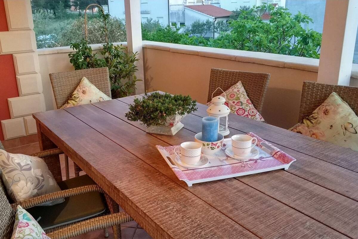 A wooden dining table with wicker chairs, a potted plant, and a tray with cups and a candle.