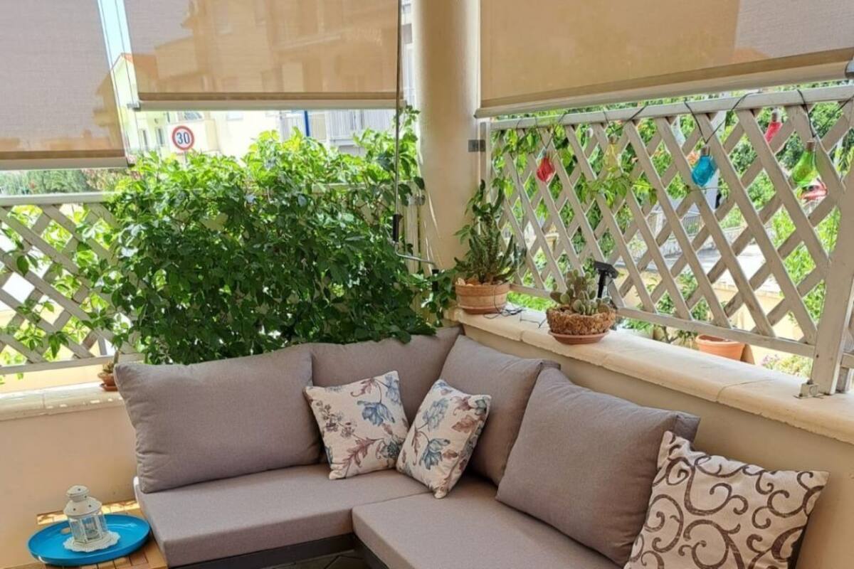 A modern outdoor seating area with a sofa, two wooden tables, and a potted plant.