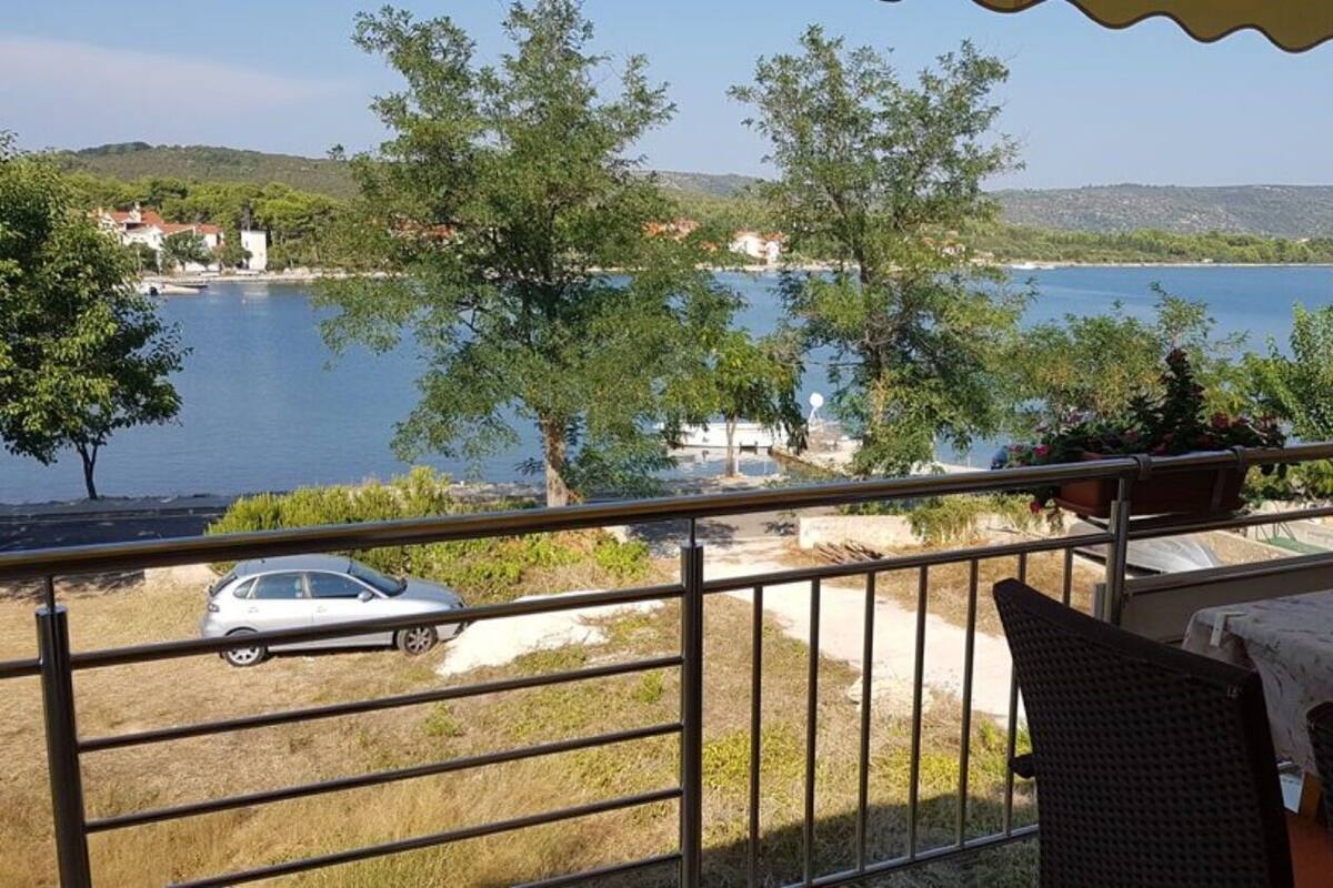 A balcony with a view of a lake, a parked car, and a table with a floral tablecloth.